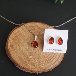 以下が含まれることがあります： スターリングシルバーのジュエリーセット。ペンダントネックレスと、お揃いのイヤリングが含まれています。ペンダントとイヤリングは、赤茶色の琥珀のような石を使用した涙の形をしています。イヤリングは「STERLING SILVER」と書かれた白いカードに展示されています。