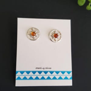 May include: A pair of sterling silver stud earrings. Each earring features a circular design with a compass rose pattern and a central amber-colored stone. The earrings are displayed on a white card with the text "Sterling Silver".