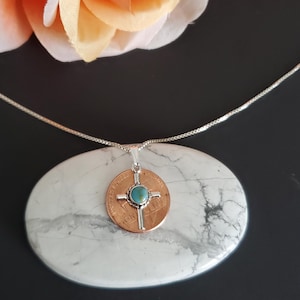 May include: A silver chain necklace with a pendant featuring a copper coin with a silver cross and a turquoise stone in the centre.