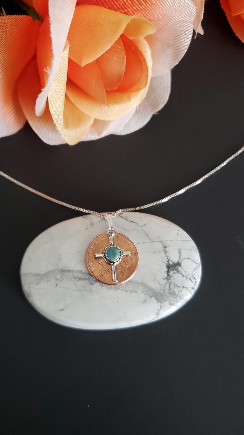 May include: A silver chain necklace with a pendant featuring a copper coin with a silver cross and a turquoise stone in the centre.