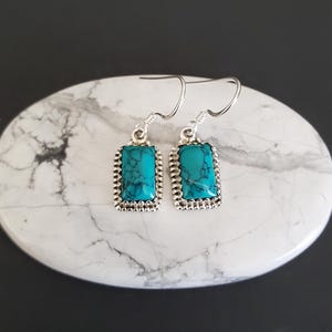 Puede incluir: Un par de pendientes de plata con piedras turquesa. Las piedras son rectangulares y tienen un patrón de mármol. Los pendientes tienen un borde de cuentas.
