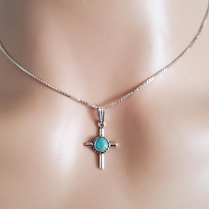 May include: A silver chain necklace with a turquoise cross pendant.