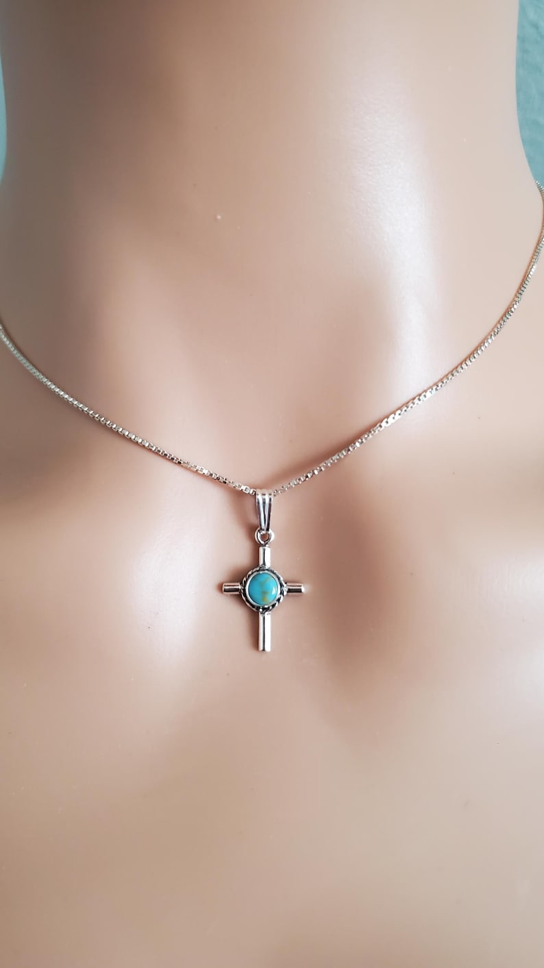 May include: A silver chain necklace with a turquoise cross pendant.
