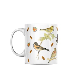 May include: White ceramic mug featuring a colourful illustration of four birds, including a greenfinch, a brambling, a linnet, and a goldfinch. The birds are depicted on branches with small orange berries and pine cones. The mug has a handle and the words "Greenfinch", "Brambling", "Linnet", and "Goldfinch" are written next to each bird.