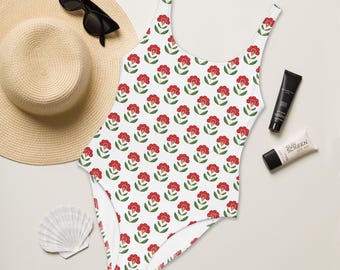 Pode incluir: Maiô branco de uma peça com estampa floral vermelha. O maiô tem decote redondo e alças finas.
