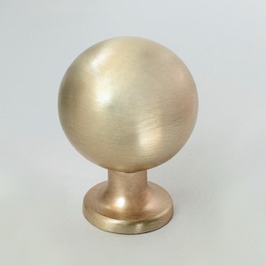 May include: A brushed gold round cabinet knob with a spherical top and a round base.