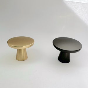 May include: Two cabinet knobs, one gold and one black, with a mushroom-shaped design. The knobs are made of metal and have a smooth, polished finish.