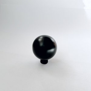 May include: A black round cabinet knob with a smooth, shiny finish.