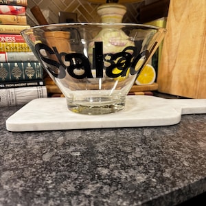 Puede incluir: Un bol de ensalada de vidrio transparente con la palabra "Salad" impresa en negro en el lateral.