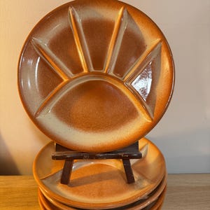 May include: A set of six vintage ceramic serving plates. Each plate is divided into sections, with a sunburst design. The plates have a glossy finish and a colour gradient from light beige to a warm orange-brown.