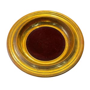 May include: A round, antique-style decorative dish with a gold-colored rim and a deep burgundy velvet center. The dish has a slightly raised edge and a smooth, polished finish. The overall design is simple yet elegant.