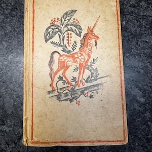 May include: Vintage book with a tan cover and a red border. The cover features a red and black illustration of a unicorn with a horn, standing in front of a stylized tree. The book shows signs of wear.