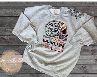 May include: Gray sweatshirt with a colorful graphic of a skull with a brain inside. The text "Running on Chaos, Brain Fog & 5% Low" is printed below the skull.