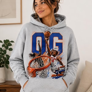 May include: A heather gray hooded sweatshirt featuring a large graphic print of a basketball player dunking a ball into a hoop. The design includes the letters OG in blue, the text New York, and the words Hustle Heart in orange and blue colors.