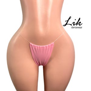Può includere: Lingerie rosa trasparente con un design a bretelle sottili. La lingerie è realizzata in un tessuto morbido ed elastico e ha un taglio a vita bassa. Il nome del marchio "Lik dancewear" è stampato sul lato destro dell'immagine.