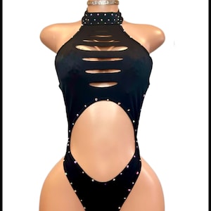 Könnte beinhalten: Schwarzer Neckholder-Body mit Cut-Out-Details und Strassverzierungen. Der Body hat einen hohen Ausschnitt und einen großen Taillenausschnitt. Strasssteine sind um den Ausschnitt, die Taille und die Beinöffnungen angeordnet. Ein Strass-Choker ist ebenfalls enthalten.