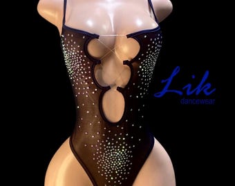 Può includere: Body nero con abbellimenti scintillanti e dettagli ritagliati. L'indumento presenta spalline sottili e il testo "Lik dancewear" in blu. Il body è esposto su un manichino.