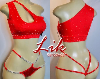 Può includere: Top rosso a spalla unica con strass e intimo rosso abbinato con un dettaglio a catena argentata. L'intimo ha un design incrociato nella parte anteriore e posteriore. Il testo "Lik dancewear" è visibile nell'immagine.