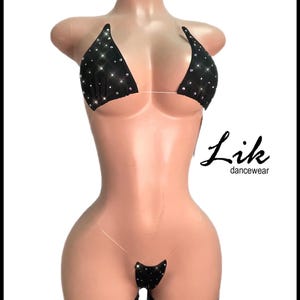 Könnte beinhalten: Schwarzes Bikini-Set mit Strasssteinen. Das Oberteil ist im Triangel-Stil mit transparenten Trägern, und das Unterteil ist ein String. Das Set wird auf einer Schaufensterpuppe präsentiert. Der Text "Lik dancewear" befindet sich unten rechts.