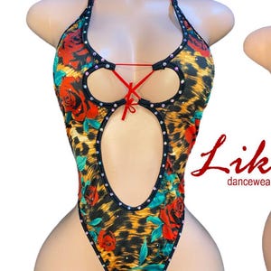 May include: A one-piece dancewear bodysuit with a leopard print and red rose pattern. The halter-style top has a red lace-up detail and is embellished with rhinestones. The bodysuit has a high-cut leg.