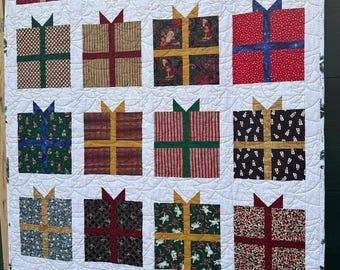 May include: A white quilt with a patchwork design of 16 different Christmas gift boxes. Each box has a different pattern and color, including red, green, blue, gold, and white.