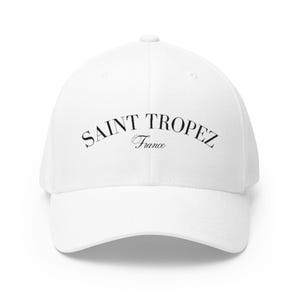 Op de afbeelding: Een witte baseballpet met een gebogen klep. De pet heeft de tekst "SAINT TROPEZ France" in zwarte letters, gebogen over de voorkant. De pet is gemaakt van een gladde stof en heeft een gestructureerd ontwerp.