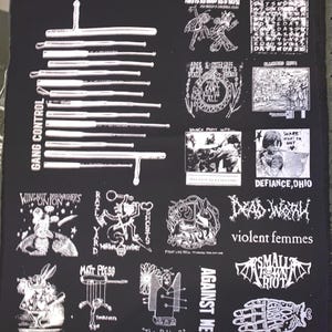May include: Black fabric panel featuring white graphic designs and text. Designs include band logos, illustrations, and the text "GANG CONTROL" and "AGAINST ME!". The panel has a variety of punk rock and alternative music themes.