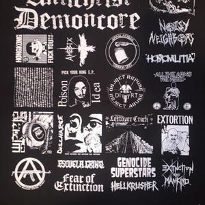 May include: Black graphic tee featuring multiple band logos and text, including "Antichrist Demoncore," "Noisy Neighbors," and "Extinction of Mankind." The design is in white, with a distressed, vintage aesthetic.