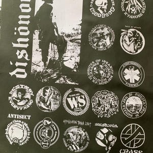 May include: Black fabric featuring white graphic designs and text. The main text reads "dishonor" in a bold, stylized font. Numerous circular patches with band logos and phrases like "Crass" and "Antisect" are also visible.