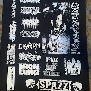May include: Black and white patch with band logos, including Magrudergrind, Shooting Spree, Skit System, Stapled Shut, Disarm, Sordo, Spazz, Iron Lung, Charles Bronson, Discharge, and Neanderthal.