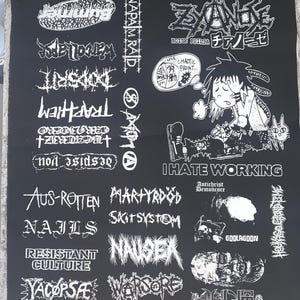 May include: Black fabric with white graphic designs. The design includes band names like "Napalm Raid", "Aus-Rotten", and "Nails". A cartoon figure with the text "I Hate Working" is also featured.