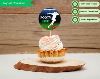 May include: A cupcake with white frosting and colorful sprinkles, topped with a circular football-themed cake topper. The topper features a football player silhouette, the words "FOOTY LIFE", and a football graphic. The cupcake sits on a wooden slice.