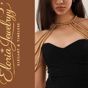 Puede incluir: Joyas doradas con cuentas para los hombros sobre un vestido negro. Las joyas están hechas de pequeñas cuentas redondas y cuelgan en múltiples hebras. El texto "Eloria Jewelryy Elegant & Timeless" está sobre un fondo marrón.