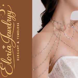 Könnte beinhalten: Eine silberne Körperkette mit mehreren Strängen aus zarten, funkelnden Kristallen. Der Schmuck drapiert sich über Schultern und Brust. Der Markenname "Eloria Jewelryy" ist in goldener Schrift auf braunem Hintergrund dargestellt.