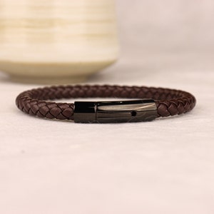 May include: A brown leather braided bracelet with a black metal clasp.