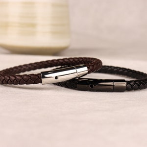 May include: Two braided leather bracelets with metal clasps. One bracelet is brown and the other is black.