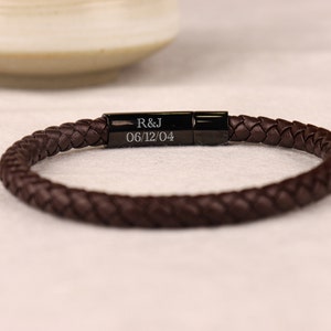May include: A brown leather braided bracelet with a black metal clasp. The clasp is engraved with the initials "R&J" and the date "06/12/04".