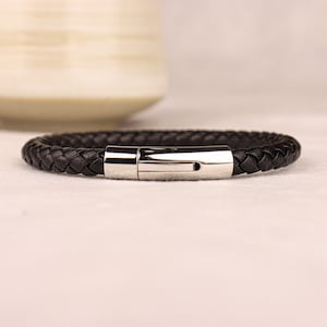 May include: A black leather braided bracelet with a silver clasp.
