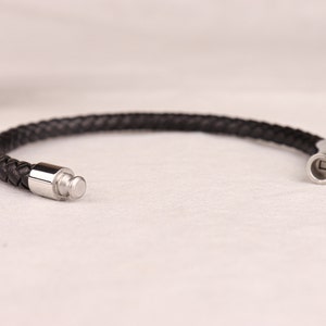 May include: A black leather bracelet with a silver clasp and a silver push button closure.
