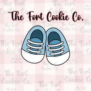 May include: A pair of light blue sneakers with white laces and soles. The shoes are a cartoon illustration, perfect for cookie cutters. The text "The Fort Cookie Co." is at the top.