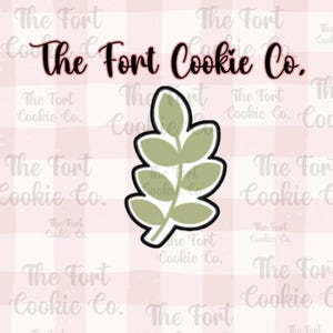 May include: A green leaf cookie cutter with a simple design. The cutter is on a pink and white gingham background. The text "The Fort Cookie Co." is visible in the background.