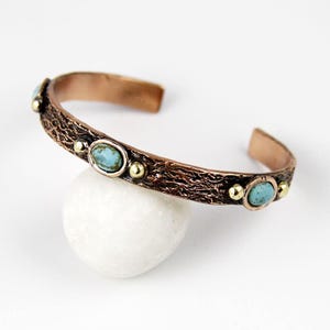 May include: A copper bracelet with a textured finish and turquoise stones set in gold accents.