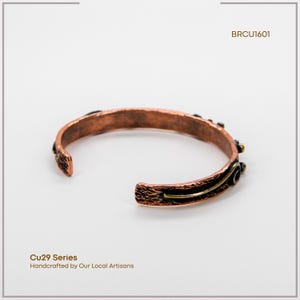 May include: Copper cuff bracelet with textured details and a dark patina. The open-ended design features decorative accents and a contrasting gold-coloured stripe. The bracelet is part of the Cu29 Series, handcrafted by local artisans.