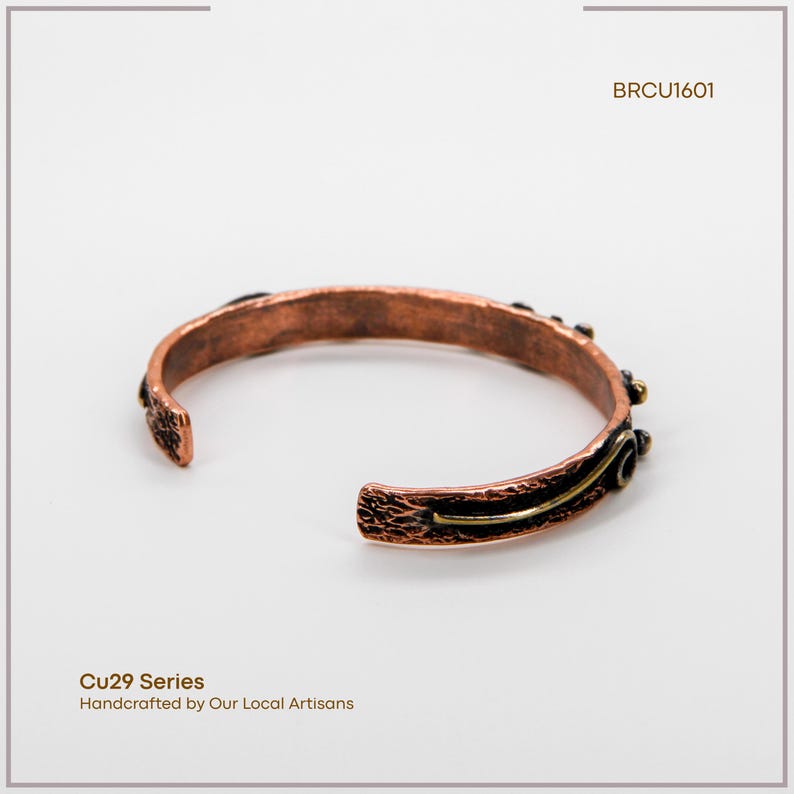 May include: Copper cuff bracelet with textured details and a dark patina. The open-ended design features decorative accents and a contrasting gold-coloured stripe. The bracelet is part of the Cu29 Series, handcrafted by local artisans.