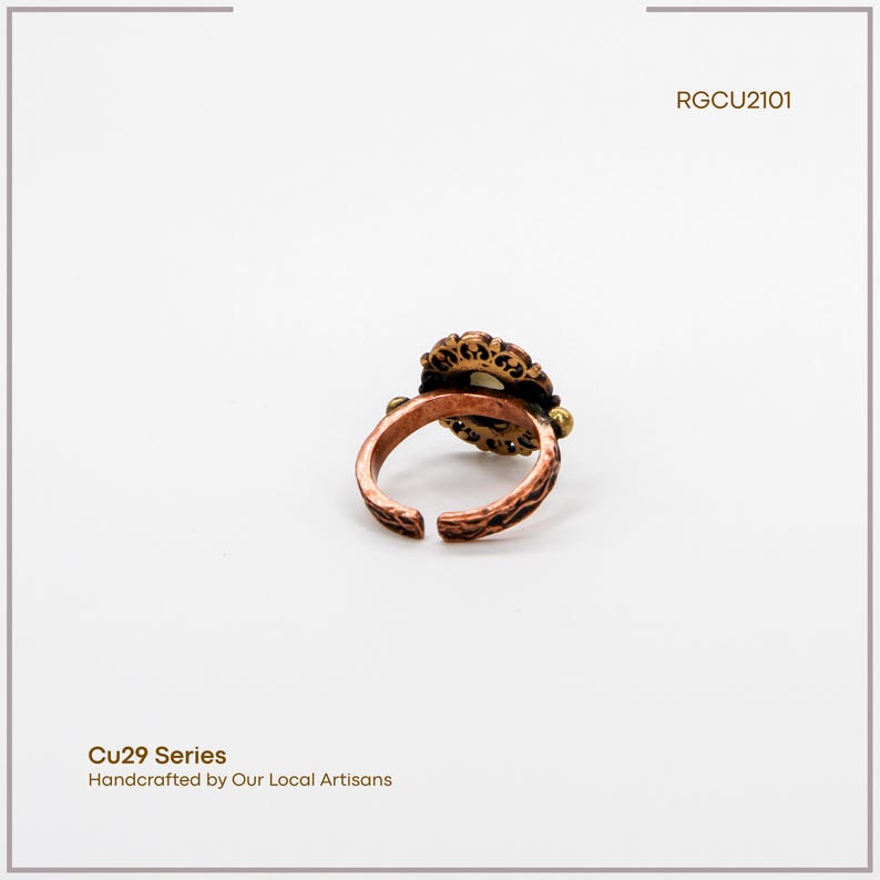 Puede incluir: Un anillo de color cobre con un dise&ntilde;o ornamentado de inspiraci&oacute;n floral. El anillo presenta una piedra central rodeada por un engaste de filigrana detallado. La banda tiene un patr&oacute;n texturizado. El texto "Cu29 Series" y "Handcrafted by Our Local Artisans" es visible.