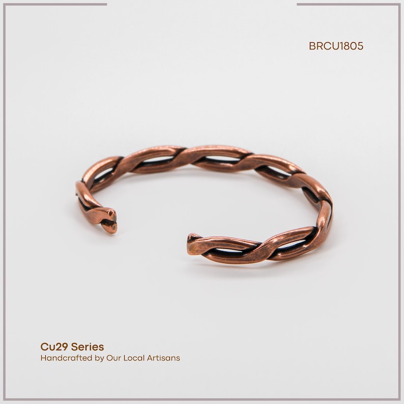 K&ouml;nnte beinhalten: Ein kupferfarbenes, offenes Armband mit geflochtenem Design. Das Armband besteht aus ineinander verschlungenen Metallstr&auml;ngen. Der Text "BRCU1805" und "Cu29 Series Handcrafted by Our Local Artisans" ist zu sehen.