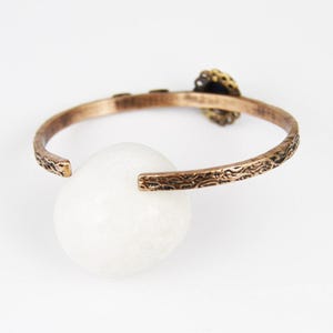 May include: A copper bracelet with an ornate design and a blue gemstone accent.