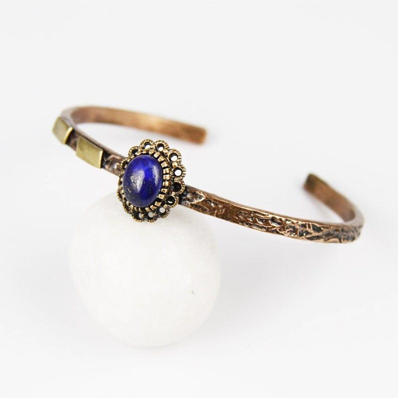 May include: A copper bracelet with a textured finish and a lapis lazuli gemstone set in a gold-toned filigree setting.