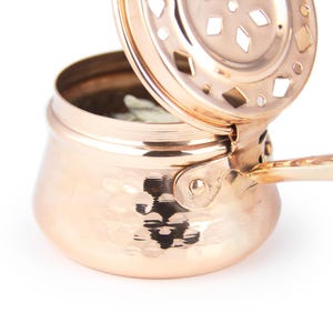 May include: A hammered copper incense burner with a hinged lid and a handle. The lid has a decorative cut-out design.