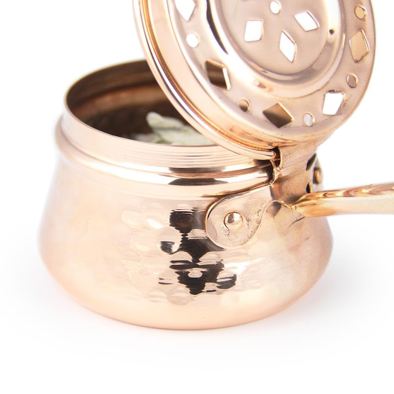 May include: A hammered copper incense burner with a hinged lid and a handle. The lid has a decorative cut-out design.